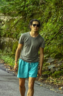 Temiz havada yürü. Gözlüklü genç bir adam çevresindeki doğaya bakar. Bir adam yolda yürüyor..