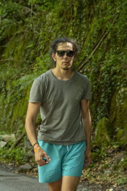 Temiz havada yürü. Gözlüklü genç bir adam çevresindeki doğaya bakar. Bir adam yolda yürüyor..