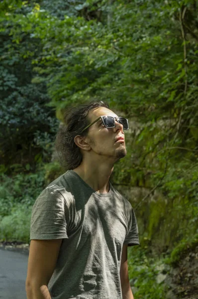 Andar ao ar livre. Um jovem de óculos de sol olha para a natureza ao seu redor. A luz do sol cai no rosto . — Fotografia de Stock