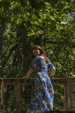 Taş bir çitte duran mavi elbiseli genç bir kız..