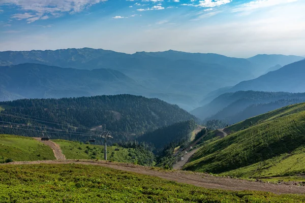 The cable car goes down from the green ridge. High mountains in the haze on the horizon.