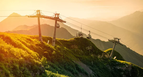 Teleferik günbatımında parlak turuncu güneş tarafından aydınlatılmış Aibga sırtta Rosa Khutor Kayak Merkezi üstündeki yaz aylarında. Krasnaya Polyana, Sochi, Rusya Federasyonu.