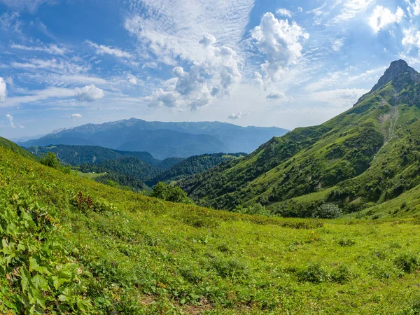 View over the Green Valley, surrounded by high mountains on a clear summer day. Krasnaya Polyana, Sochi, Caucasus, Russia.