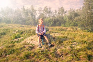 Bir sırt çantası ve trekking Polonyalılar ile bir çocuk gezgin bir taş ormanın kenarına önünde siste dinleniyor.