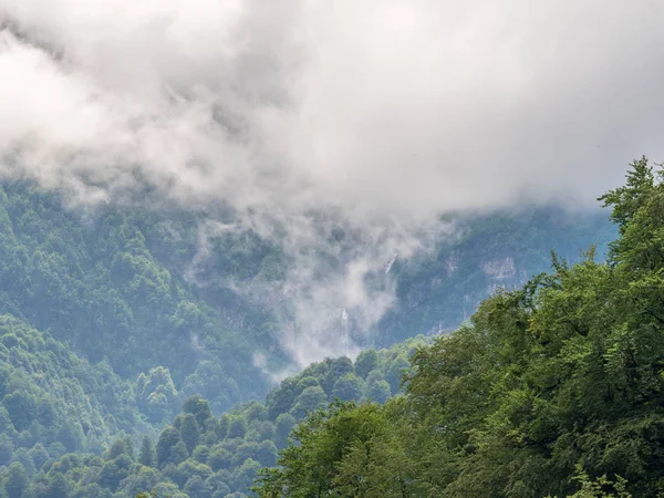 Bir şelale ve kalın sis Peaks'e yeşil dağların muhteşem manzarası.