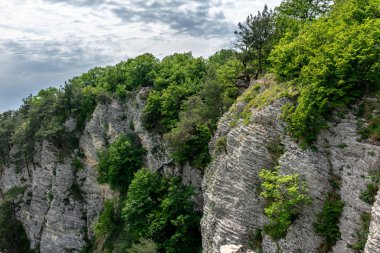 Dağ ile dik bir yeşil kayalık yamaç. Bir adam son derece bir uçurumun kenarında oturuyor.