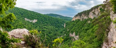 Bir dik kayalık yamaç ve kalın yeşil orman aşağıdaki Vadisi dağ manzarasına. Konut ve deniz uzaktan görülebilir.