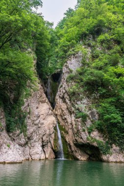 Yüksek bir şelale uçurumdan açık bir göle düşüyor. Şelale yeşil ormanıyla çevrilidir. Nehir Agura, Sochi, Rusya Federasyonu