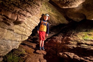 Ek aydınlatma ile taş duvarlar ile eski mağara içindeki oğlan. Bir mağarada taştan bir duvar dokusu. Çim ve moss yeraltı büyümek. Akhshtyr Mağarası, Sochi, Rusya Federasyonu