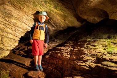 Ek aydınlatma ile taş duvarlar ile eski mağara içindeki oğlan. Bir mağarada taştan bir duvar dokusu. Çim ve moss yeraltı büyümek. Akhshtyr Mağarası, Sochi, Rusya Federasyonu
