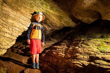Ek aydınlatma ile taş duvarlar ile eski mağara içindeki oğlan. Bir mağarada taştan bir duvar dokusu. Çim ve moss yeraltı büyümek. Akhshtyr Mağarası, Sochi, Rusya Federasyonu