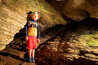 Ek aydınlatma ile taş duvarlar ile eski mağara içindeki oğlan. Bir mağarada taştan bir duvar dokusu. Çim ve moss yeraltı büyümek. Akhshtyr Mağarası, Sochi, Rusya Federasyonu