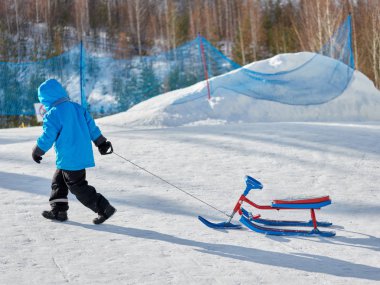 Bir çocuk kışın saf beyaz kar bir kar scooter yokuş yukarı taşır.