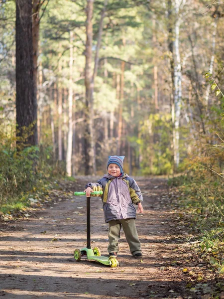 Ένα μικρό αγόρι που στέκεται με ένα σκούτερ στο πάρκο — Φωτογραφία Αρχείου