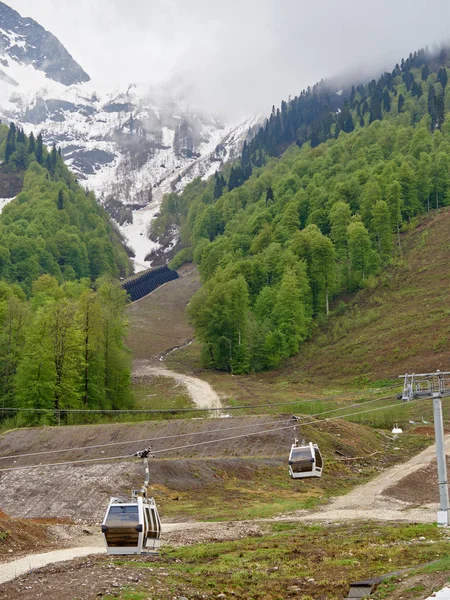 Seilbahn am Frühlingshang mit geschmolzenem Schnee. Schneebedeckte Berge im Nebel. — Stockfoto