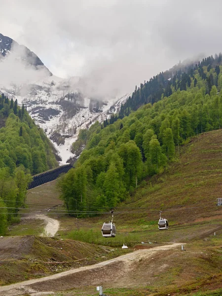 Seilbahn am Frühlingshang mit geschmolzenem Schnee. Schneebedeckte Berge im Nebel. — Stockfoto