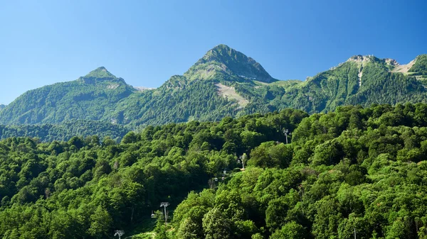 Ψηλά καταπράσινα βουνά με καλώδιο ανελκυστήρες. Γαλάζιο καθαρό ουρανό. — Φωτογραφία Αρχείου