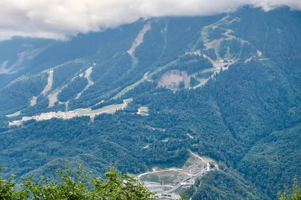 Sports facilities and residential buildings on the slope of a high mountain with a green slope and the top in the clouds. A sports and tourist base in the mountains.