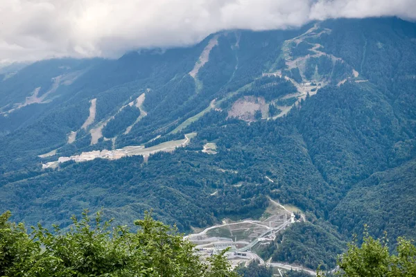 Sports facilities and residential buildings on the slope of a high mountain with a green slope and the top in the clouds. A sports and tourist base in the mountains.