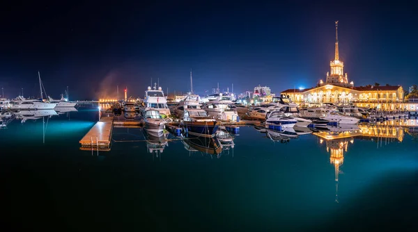 Tengeri állomás Szocsi, világító fények éjszaka tükörképe a vízben. Jachtok és csónakok a mólón. — Stock Fotó