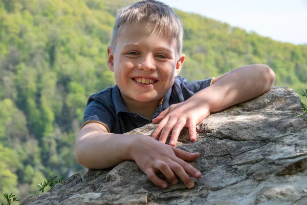 一个带着微笑的男孩旅行者爬上了悬崖的顶端 — 图库照片
