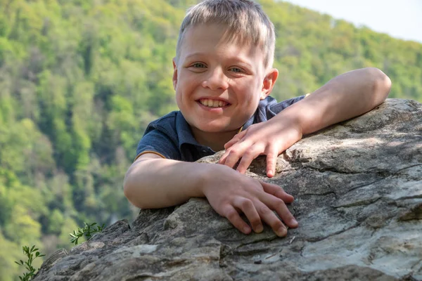 一个带着微笑的男孩旅行者爬上了悬崖的顶端 — 图库照片