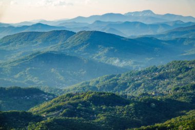 Gün batımında sis içinde dağların katmanları. Dağlarda güzel gün batımı. Ovalarda köyler ve sis ile tepelik bir vadide güzel gün batımı.