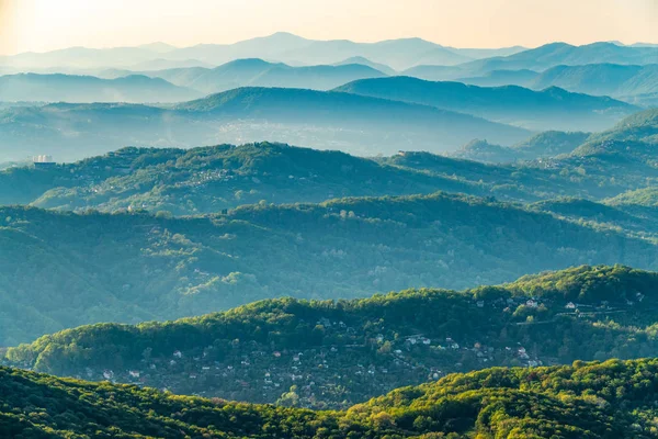 Schichten von Bergen im Dunst während des Sonnenuntergangs. wunderschöner Sonnenuntergang in den Bergen. wunderschöner Sonnenuntergang in einem hügeligen Tal mit Dörfern und Nebel im Tiefland. — Stockfoto