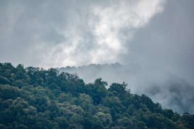 Ormanlı yamaçlarda ve bulutlarda gizlenmiş doruklara sahip yüksek dağlar.