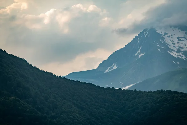 Cordilheiras com encostas verdes e rochosas. Montanhas com picos nevados escondidos nas nuvens . — Fotografia de Stock
