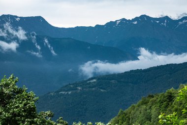 Ormanlı yamaçlarda ve bulutlarda gizlenmiş doruklara sahip yüksek dağlar.