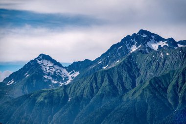 Yeşil yamaçlara ve karlı doruklara sahip yüksek dağlar.