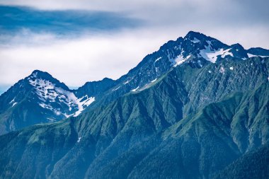 Yeşil yamaçlara ve karlı doruklara sahip yüksek dağlar.