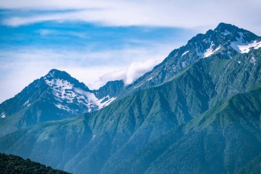 Yeşil yamaçlara ve karlı doruklara sahip yüksek dağlar.