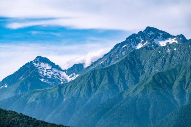 Yeşil yamaçlara ve karlı doruklara sahip yüksek dağlar.