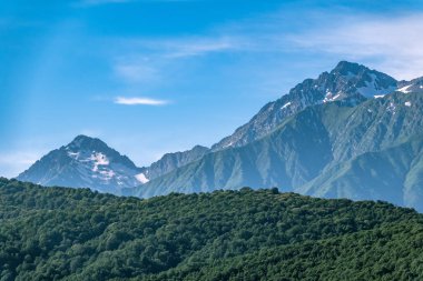 Yeşil yamaçlara ve karlı doruklara sahip yüksek dağlar.