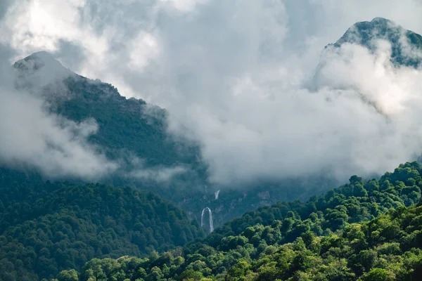 Montanhas verdes com uma alta cachoeira em nevoeiro e nuvens . — Fotografia de Stock