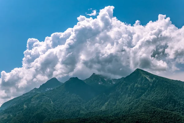 Cordilheiras com encostas verdes e rochosas. Montanhas com picos nevados escondidos nas nuvens . — Fotografia de Stock