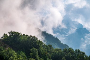Ormanlı yamaçlarda ve bulutlarda gizlenmiş doruklara sahip yüksek dağlar.