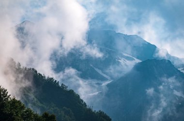 Ormanlı yamaçlarda ve bulutlarda gizlenmiş doruklara sahip yüksek dağlar.