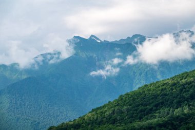 Yeşil yamaçlarda ve bulutlu yaz gününde yüksek dağların kayalık doruklarına