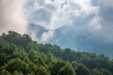 Ormanlı yamaçlarda ve bulutlarda gizlenmiş doruklara sahip yüksek dağlar.