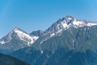 Yeşil yamaçlara ve karlı doruklara sahip yüksek dağlar.