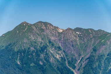 Yeşil yamaçlara ve karlı doruklara sahip yüksek dağlar.