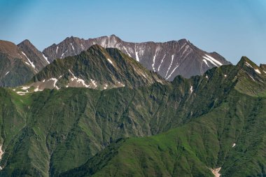 Yeşil yamaçlara ve karlı doruklara sahip yüksek dağlar.