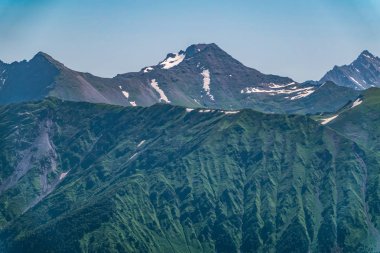 Yeşil yamaçlara ve karlı doruklara sahip yüksek dağlar.