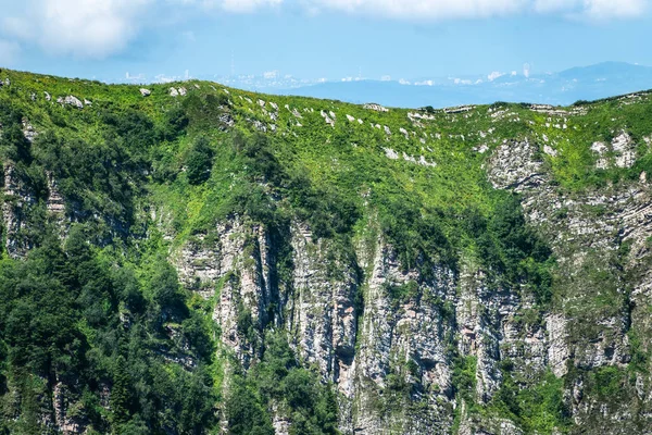 Açık mavi gökyüzüne karşı kayalar ve ağaçlar ile dağ sırası. Bir dağ zirvesinden sis mesafede şehrin görünümü.