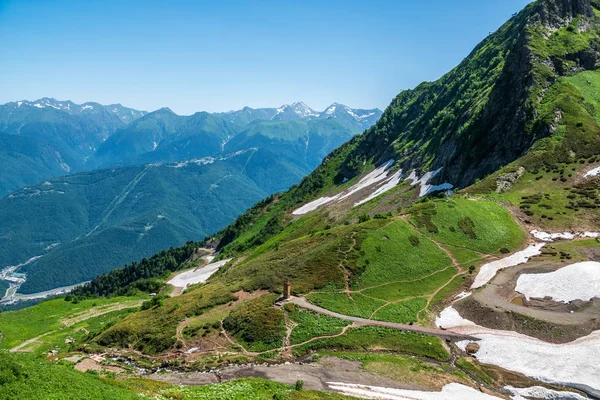 Yeşil yamaçlara ve karlı doruklara sahip yüksek dağlar.