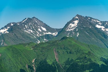 Yeşil yamaçlara ve karlı doruklara sahip yüksek dağlar.
