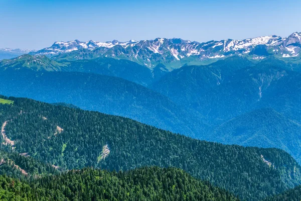 Yüksek dağlarla çevrili yeşil dağ vadisine yükseklikten görünümü. Ufukta karla kaplı dağ zirveleri. Krasnaya Polyana, Soçi, Kafkasya, Rusya Federasyonu.